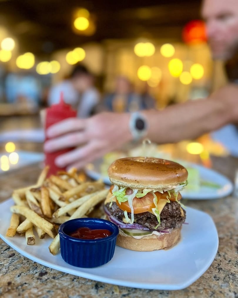 A double cheeseburger with lettuce, tomato, and onion, served with fries and ketchup on a white plate.