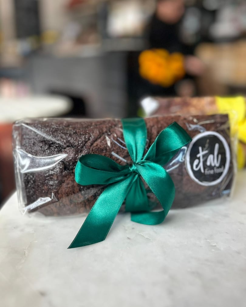 Chocolate loaf cake wrapped in plastic with a green ribbon and an "et al fine food" sticker.